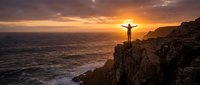 Person with arms raised celebrating freedom on dramatic coastal cliff at golden sunset over ocean waves.