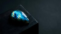 Polished labradorite gemstone with brilliant blue flash on dark slate surface showcasing natural iridescent colors and mineral beauty for jewelry design.