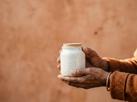 Person with dark skin tone holding a ceramic jar with white glaze against a warm terracotta background, showcasing artisanal pottery and handcrafted ceramics for retail or craft business use.
