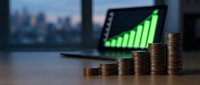 Stacked coins showing financial growth with upward trending graph on laptop screen and city skyline in background, representing business success and investment returns.