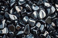 Polished black obsidian stones with silvery reflections create abstract pattern background. Natural volcanic glass pieces showcase glossy surface and sharp edges.