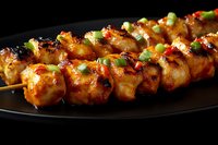 Grilled chicken skewers with spicy glaze and green onions on black plate. Juicy meat pieces charred and glazed with Asian-inspired marinade, garnished with scallions.