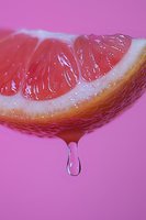 Fresh grapefruit slice with juice drop falling against pink background, macro close-up showing detailed pulp texture and citrus segments in vibrant colors.
