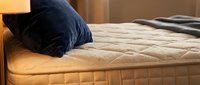 Comfortable bed with quilted mattress and navy blue pillow in warm bedroom lighting, suitable for home decor and furniture marketing.