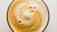 Overhead view of creamy coffee or cappuccino with rich foam and bubbles in glass cup, isolated on white background for beverage and cafe design use.