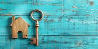 Vintage brass key with house-shaped keychain on turquoise weathered wooden background. Real estate concept symbolizing home ownership and property investment.