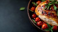 Juicy grilled chicken breast with roasted cherry tomatoes and fresh rosemary served in rustic ceramic bowl on dark background. Food photography for restaurant menu.