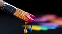 Vibrant paint drips from artistic paintbrush with colorful drops falling against dark background, showing rainbow colors merging in creative motion capture.