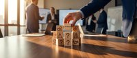 Businessman hand arranging wooden blocks with question marks on office desk during team meeting for problem solving and decision making concepts.