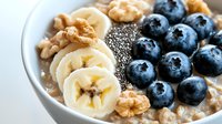 Nutritious breakfast bowl with fresh blueberries, sliced banana, chia seeds and walnuts on creamy oatmeal porridge, closeup view of healthy morning meal.