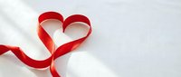 Red satin ribbon shaped into heart symbol on white background with soft shadows, perfect for Valentine's Day cards, wedding invitations and romantic designs.