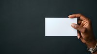 Close-up of male hand with dark skin tone holding blank white business card against dark background, suitable for corporate branding and identity design.