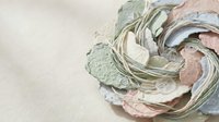 Delicate paper flower with layered petals in soft pastel colors of green, pink and cream creating an elegant handmade craft decoration on neutral background.