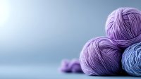 Soft wool yarn balls in purple and blue tones arranged on blurred background, creating cozy crafting atmosphere for knitting and crochet projects.