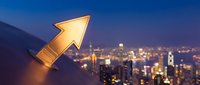Golden arrow pointing upward over illuminated city skyline at dusk representing growth, success and business progress in urban financial district.