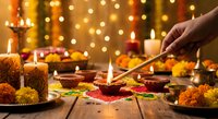 Hand lighting traditional oil lamps during Diwali celebration with marigold flowers, sweets, and warm bokeh lights creating festive atmosphere for Hindu festival.
