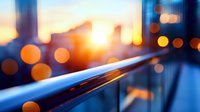 Urban sunset bokeh lights reflecting on modern glass railing with warm golden hour glow and city skyline silhouette creating atmospheric depth and contemporary architectural mood.