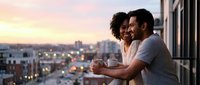 Young diverse couple enjoying coffee on urban balcony at sunset, cityscape background, lifestyle and relationship concept for advertising and editorial use.