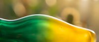 Flowing green and yellow liquid with smooth wave motion and glossy surface against soft blurred background, suitable for cosmetics, wellness, and product packaging design.