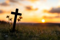 Christian cross silhouette against dramatic sunset sky with wildflowers in foreground, spiritual and peaceful scene in golden evening light. For religious designs.