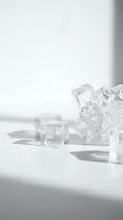 Clear crystal ice cubes scattered on white surface with dramatic shadows and natural lighting for beverage and cooling concepts.