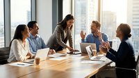 Diverse business team collaborating in modern conference room with city skyline view. Professional meeting with laptops and documents on wooden table.