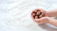 Child's hands holding macadamia nuts on marble surface, suitable for food, nutrition, healthy snacking, and cooking content.