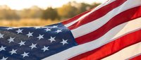 American flag waving in golden sunlight with patriotic red white and blue stars and stripes displaying national pride and freedom during sunset hour.