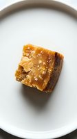 Golden caramel square pastry with sea salt crystals on white ceramic plate, overhead view. Suitable for bakery, dessert, and food styling projects.