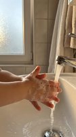 Hands washing with soap and water in modern bathroom sink with natural sunlight streaming through window for hygiene and cleanliness routine.