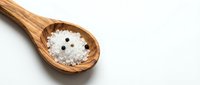 Wooden spoon filled with sea salt crystals on white background, suitable for cooking, food styling, culinary content, and wellness publications.