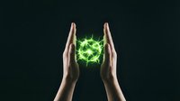Two hands holding glowing green energy sphere with electric light effect against dark background for technology and power concepts.