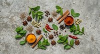 Aromatic spices and fresh herbs arranged on textured stone surface. Turmeric, cinnamon, star anise, cardamom, chili peppers and basil leaves for cooking.