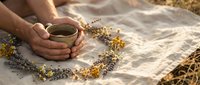 Hands holding herbal tea cup surrounded by dried chamomile flowers on linen fabric. Natural wellness and relaxation concept for spa and healthy lifestyle.