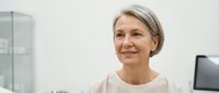 Confident mature Caucasian businesswoman with gray hair smiling in modern office environment. Professional corporate portrait for business presentations.