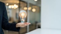 Businessman holding glowing light bulb in palm representing innovation, creativity, and bright ideas in modern office environment for business concepts.