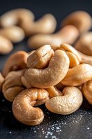 Fresh roasted cashew nuts macro shot with natural texture and salt crystals on dark background, selective focus on foreground nuts for food photography.