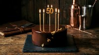 Elegant chocolate birthday cake with golden number 50 candles on rustic wooden table, dark moody atmosphere for celebration and anniversary concepts.