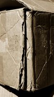 Damaged cardboard box with torn edges and deep cracks showing wear from shipping and handling in sepia tone.