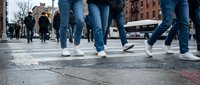 People walking across urban street intersection with legs and feet in motion showing city pedestrian traffic and daily commute in downtown area.