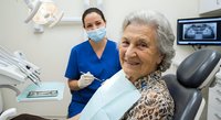 Senior woman smiling during dental checkup with female dentist in modern clinic office for oral health care and medical treatment.