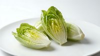 Fresh romaine lettuce hearts cut in half showing crisp green leaves and white stems on white plate, healthy vegetable ingredient for salads and cooking.