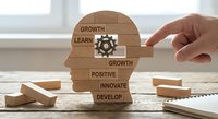 Business professional assembling wooden puzzle pieces forming human head profile with motivational words growth, learn, positive, innovate, develop.