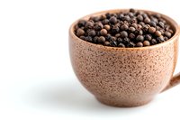 Black peppercorns in rustic ceramic cup on white background. Aromatic whole spices for cooking and seasoning, macro food photography with copy space.