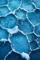 Cracked frozen lake surface with geometric pattern of broken ice pieces in deep blue tones, creating natural abstract winter texture for backgrounds.