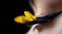 Artistic macro shot of long black eyelashes with decorative yellow butterfly wing attached, creating surreal beauty makeup look for fashion and cosmetics industry.