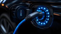 Electric vehicle charging port with glowing blue LED lights illuminating the socket and cable connector, showing modern clean energy technology in dark setting.