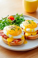 Eggs Benedict with poached eggs, bacon and hollandaise sauce on toasted bread served with fresh arugula salad and orange juice for gourmet breakfast.