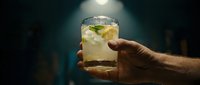 Male hand holding refreshing cocktail with ice and mint garnish in atmospheric bar lighting for beverage advertising and hospitality marketing.