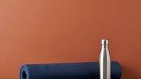 Stainless steel water bottle and rolled yoga mat on terracotta background for fitness, wellness, and healthy lifestyle marketing.